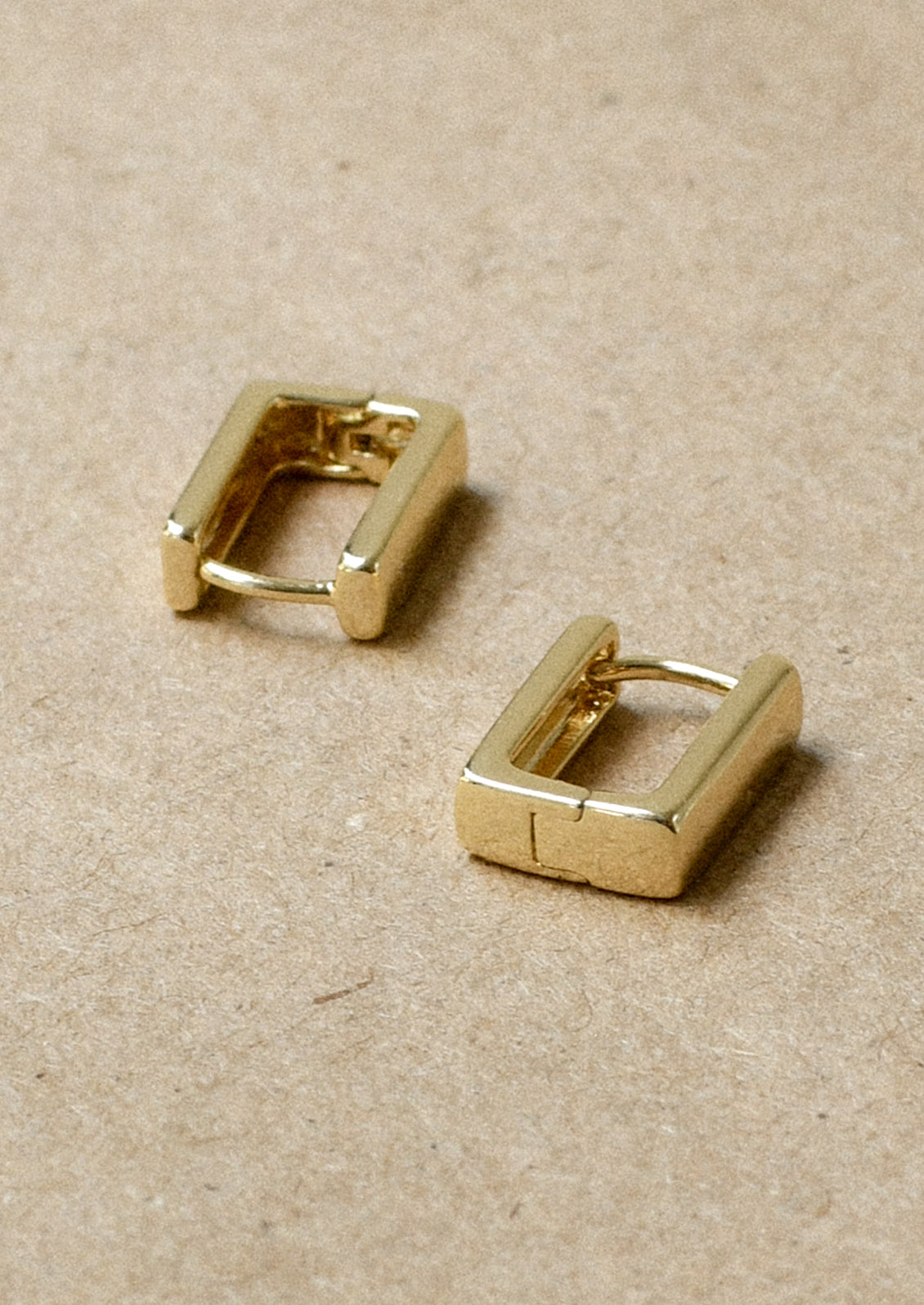 A pair of gold rectangular huggie earrings.