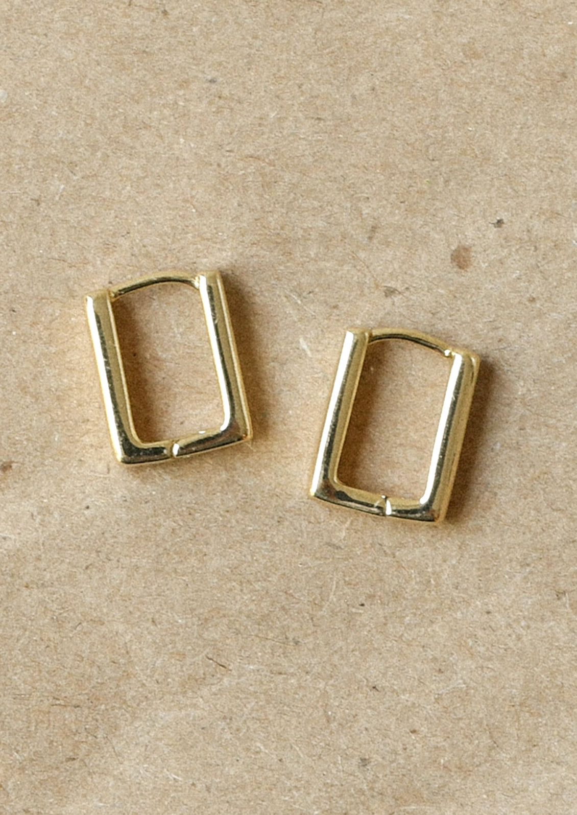 A pair of gold rectangular huggie earrings.