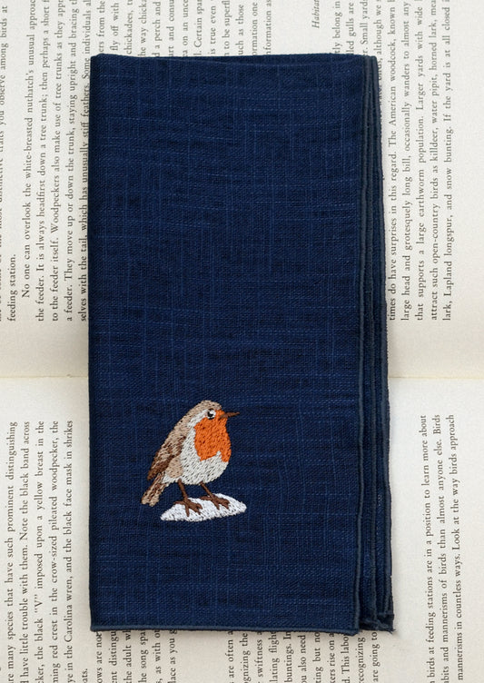 A navy blue linen napkin with tonal serged edges, and an embroidered robin at corner.