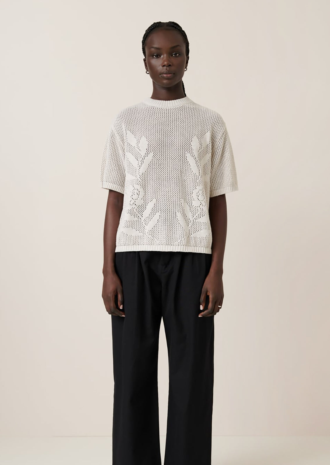 A woman wearing an open mesh knit short sleeve sweater with tonal floral motif.