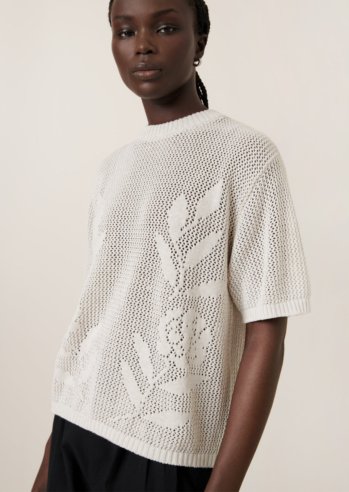 A woman wearing an open mesh knit short sleeve sweater with tonal floral motif.