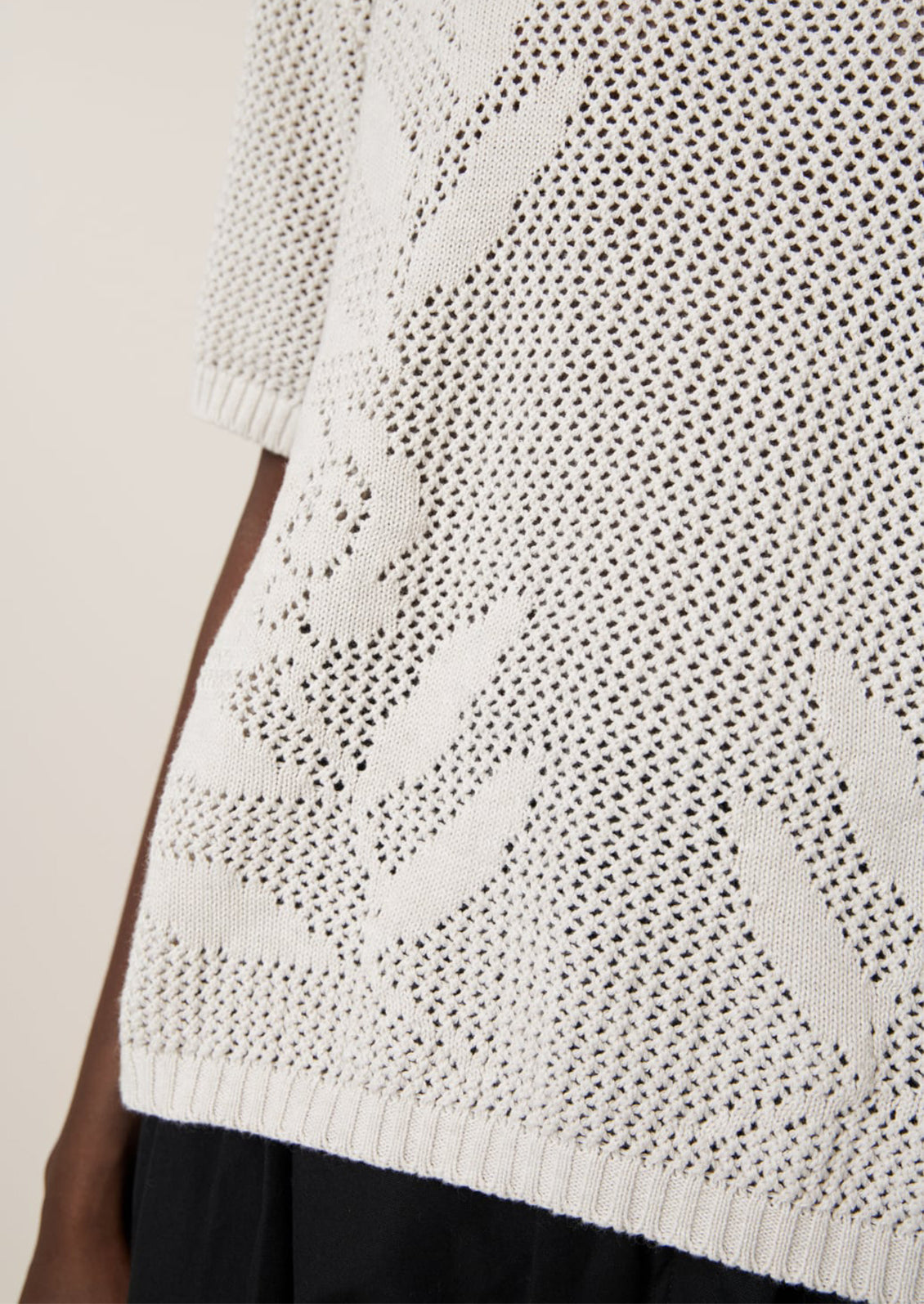 A woman wearing an open mesh knit short sleeve sweater with tonal floral motif.