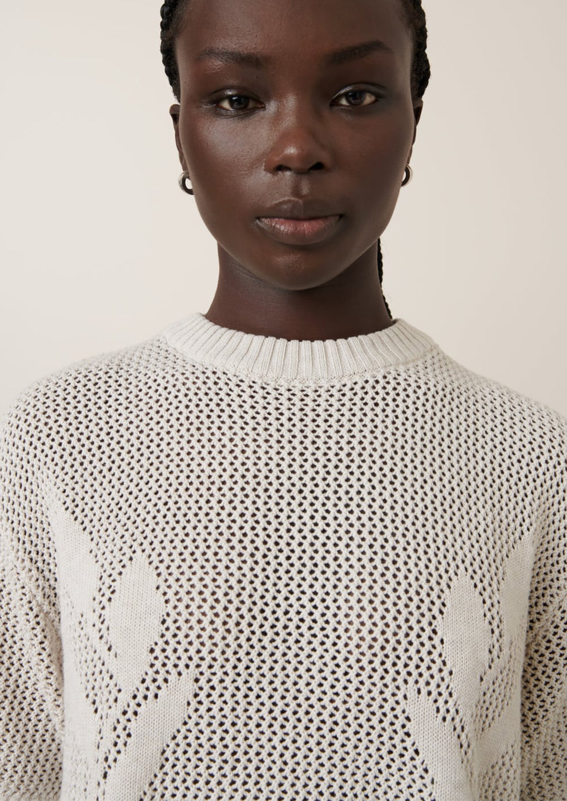 A woman wearing an open mesh knit short sleeve sweater with tonal floral motif.