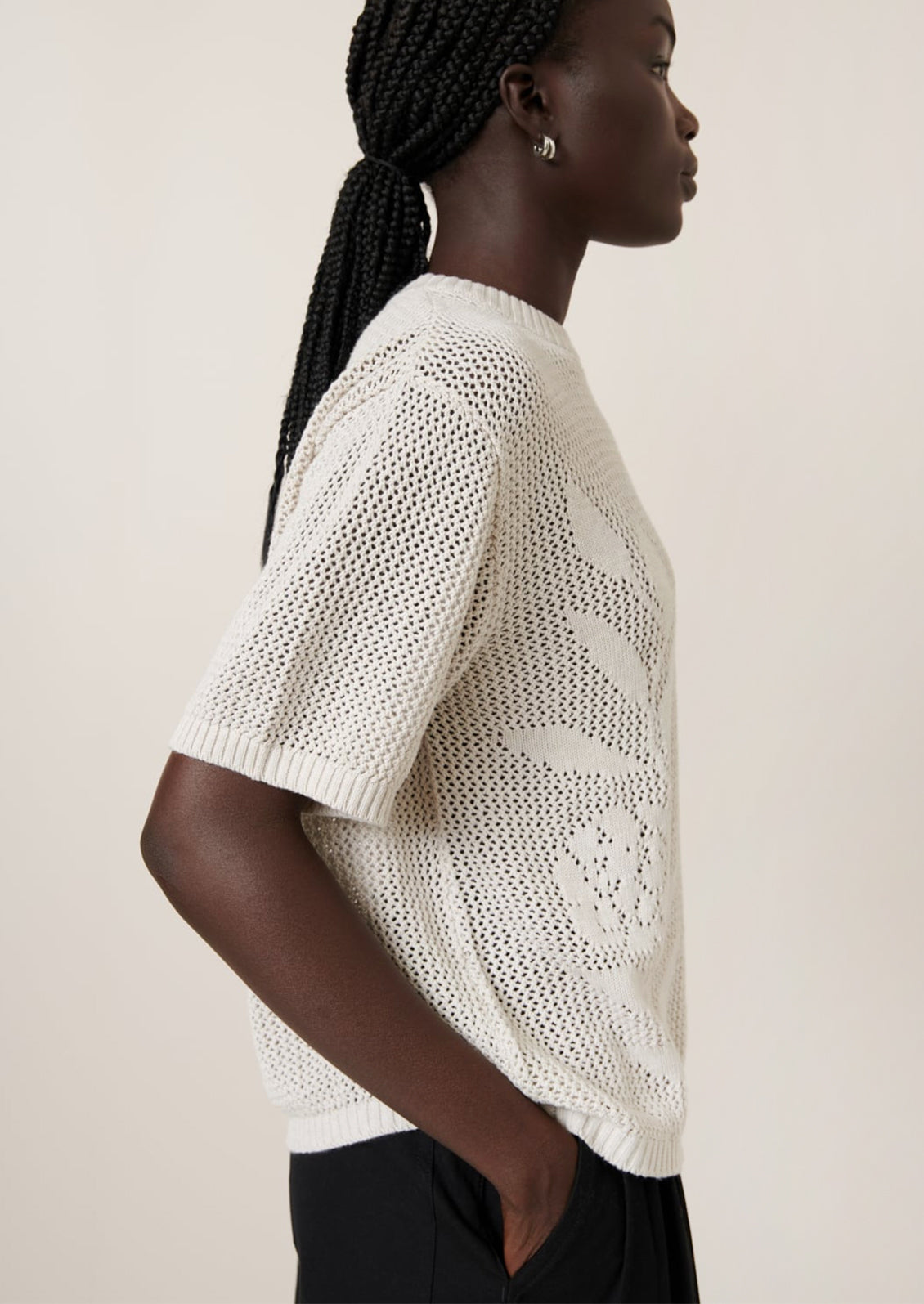 A woman wearing an open mesh knit short sleeve sweater with tonal floral motif.
