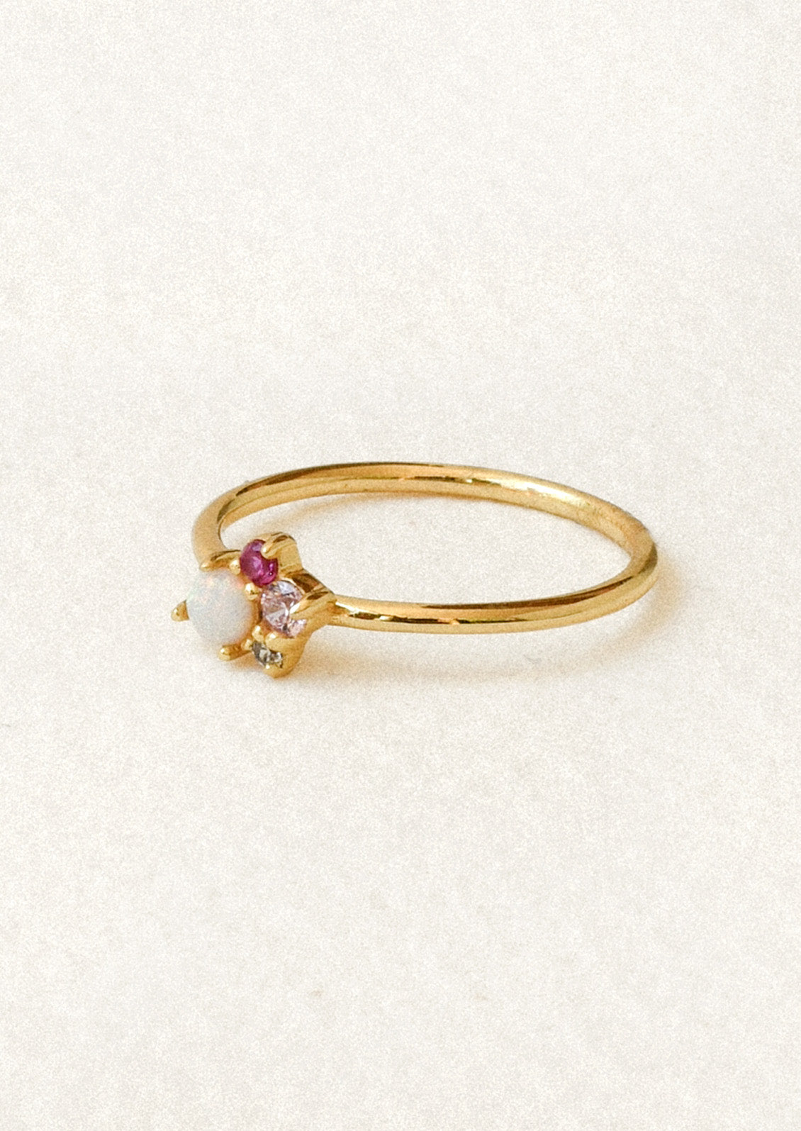 A gold ring with a cluster of gems including a simulated opal and three other small pink and clear gems.