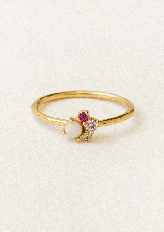A gold ring with a cluster of gems including a simulated opal and three other small pink and clear gems.