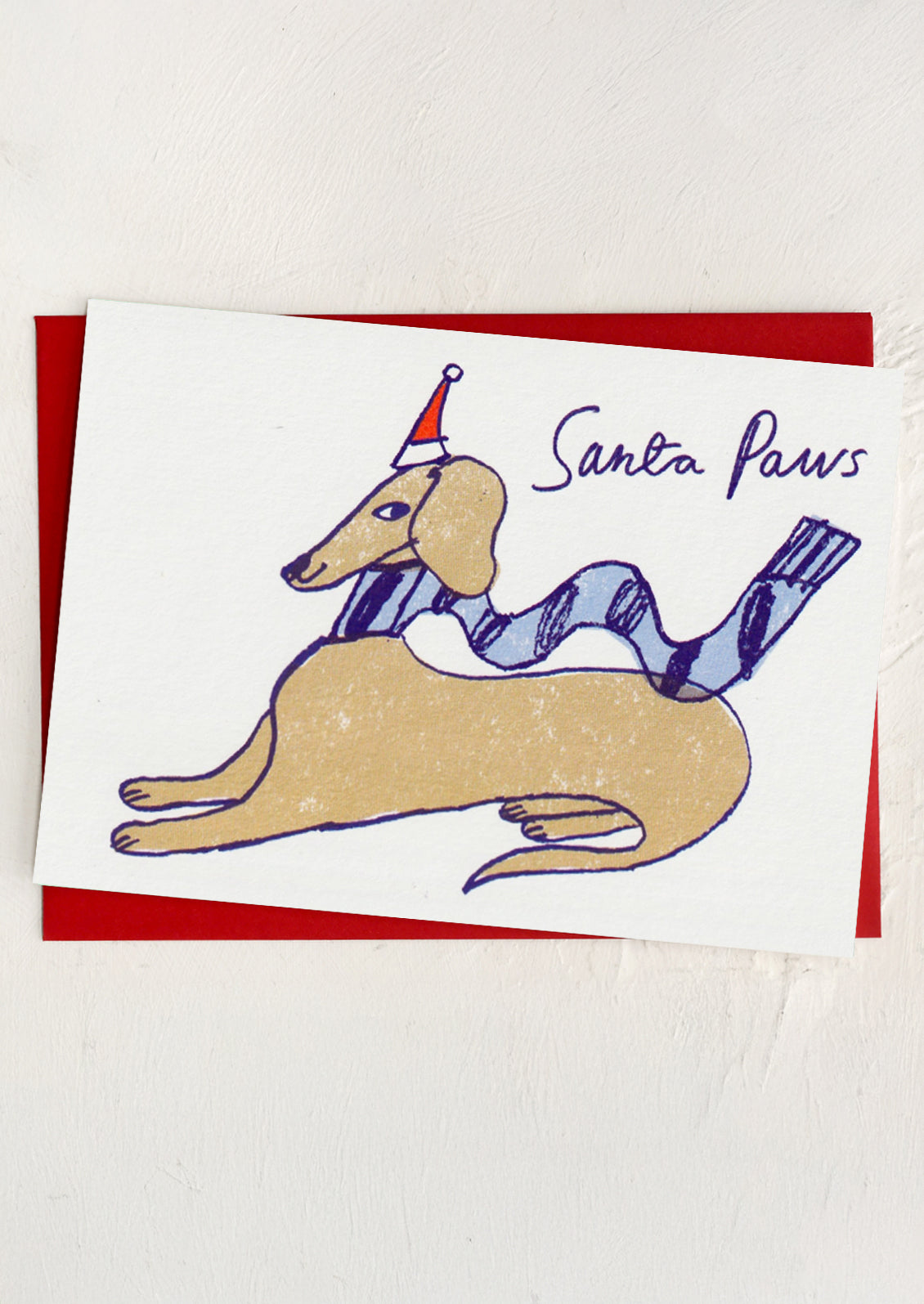 A greeting card with illustration of a brown dog wearing a Santa hat, text reads "Santa Paws"