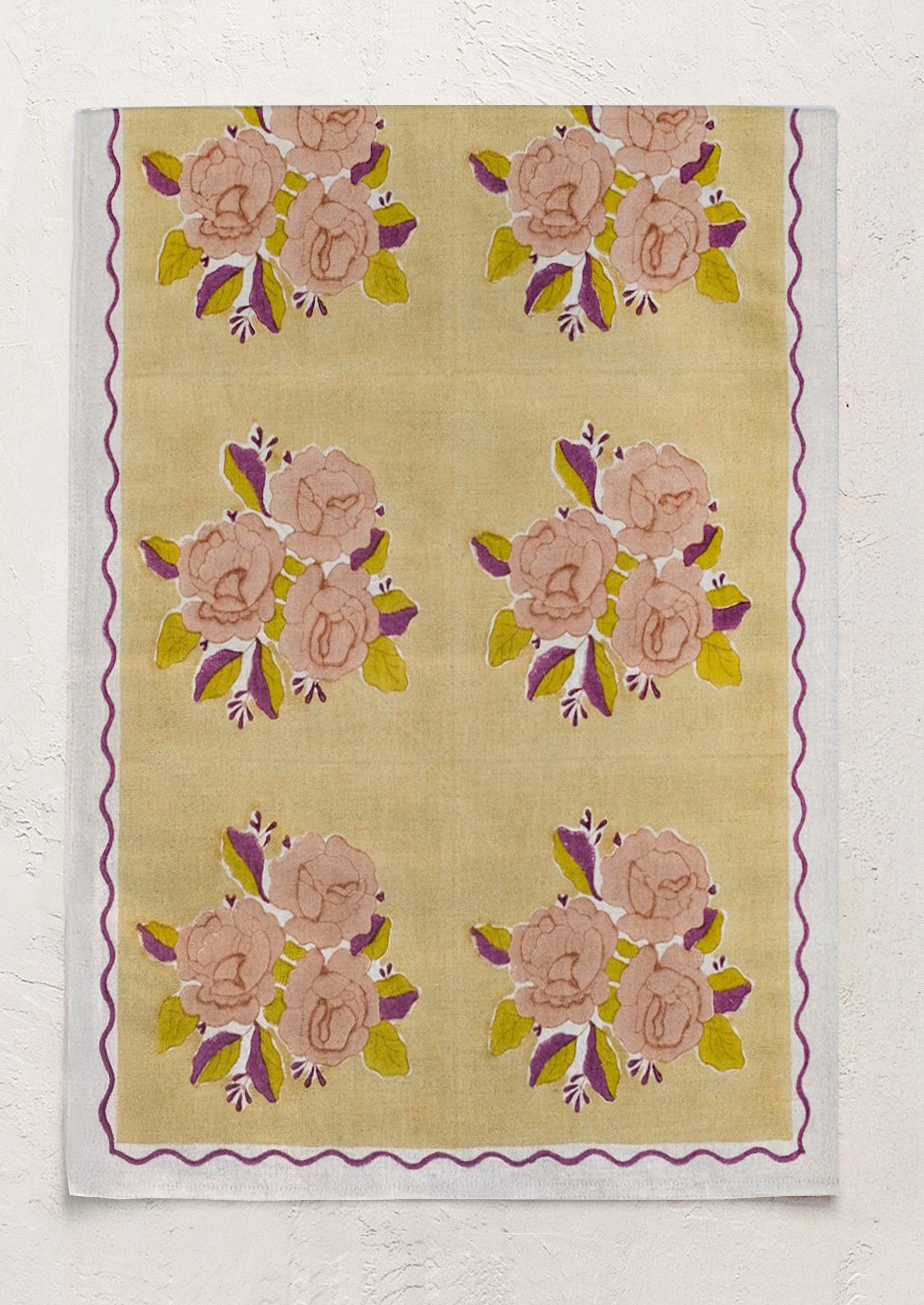 A linen table runner with pale yellow floral pattern and wavy purple border.