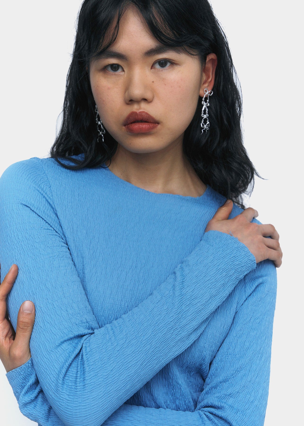 A pair of silver earrings with four bows, in slightly different shapes, stacked on top of each other.