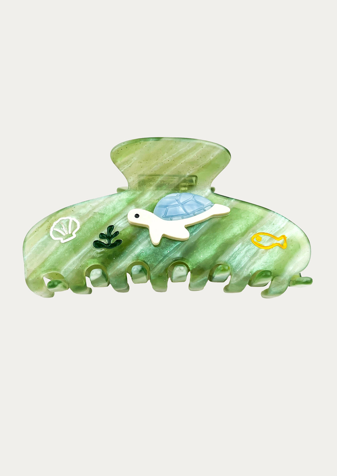A green marbled hair claw clip decorated with small sea-themed embellishments including a white turtle with a blue shell, a white seashell, green seaweed, and a yellow fish.