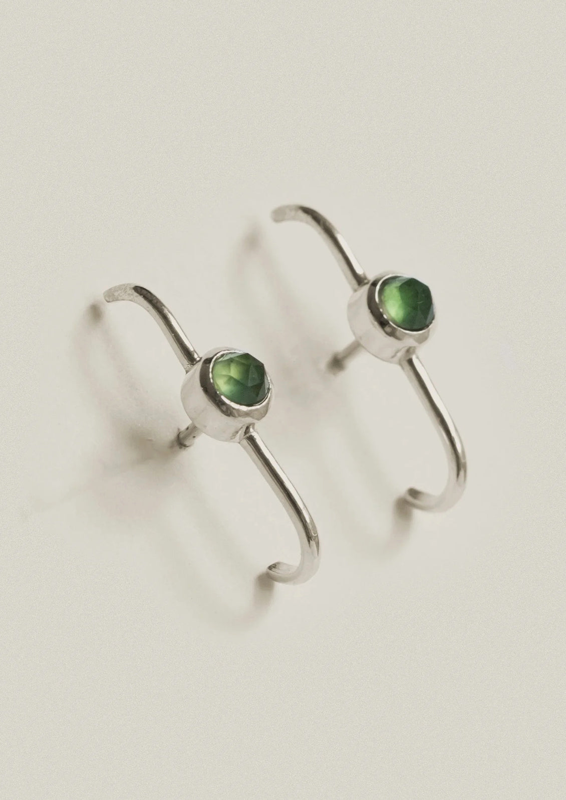A pair of sterling silver cuff earrings with green gems in the center.