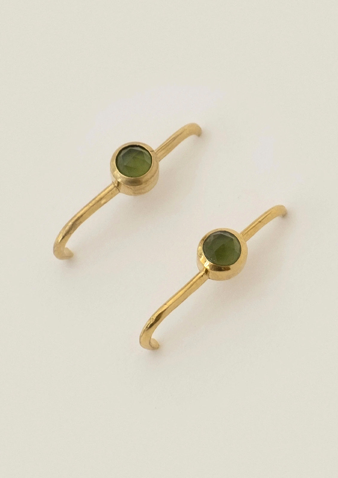 A pair of gold cuff earrings with green gems in the center.