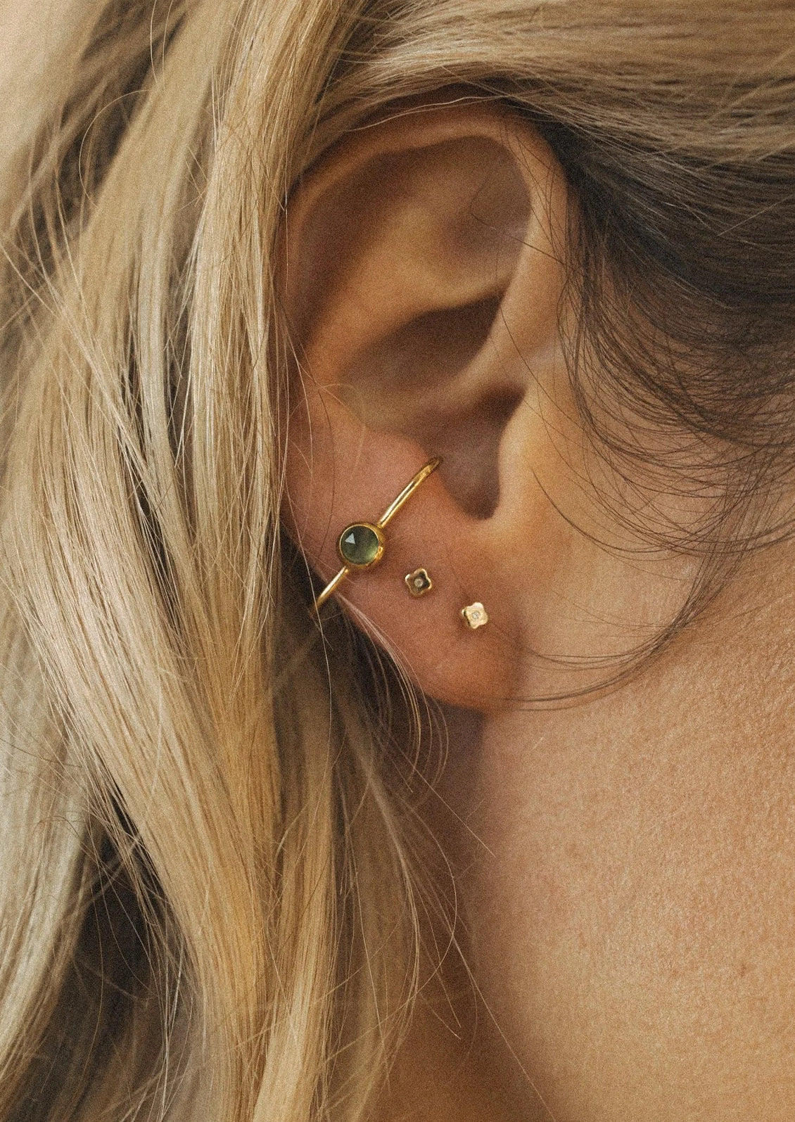 A woman wearing two small stud earrings and a cuff earring with a green gem.