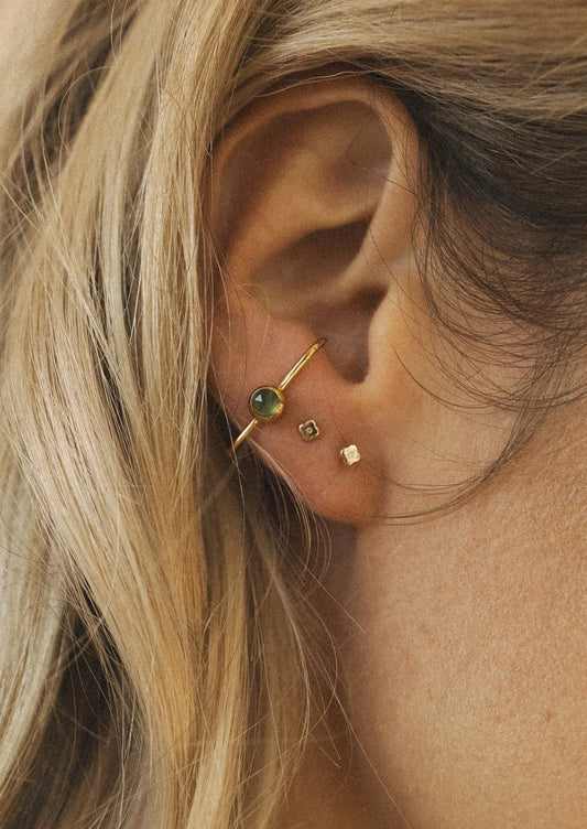 A woman wearing two small stud earrings and a cuff earring with a green gem.