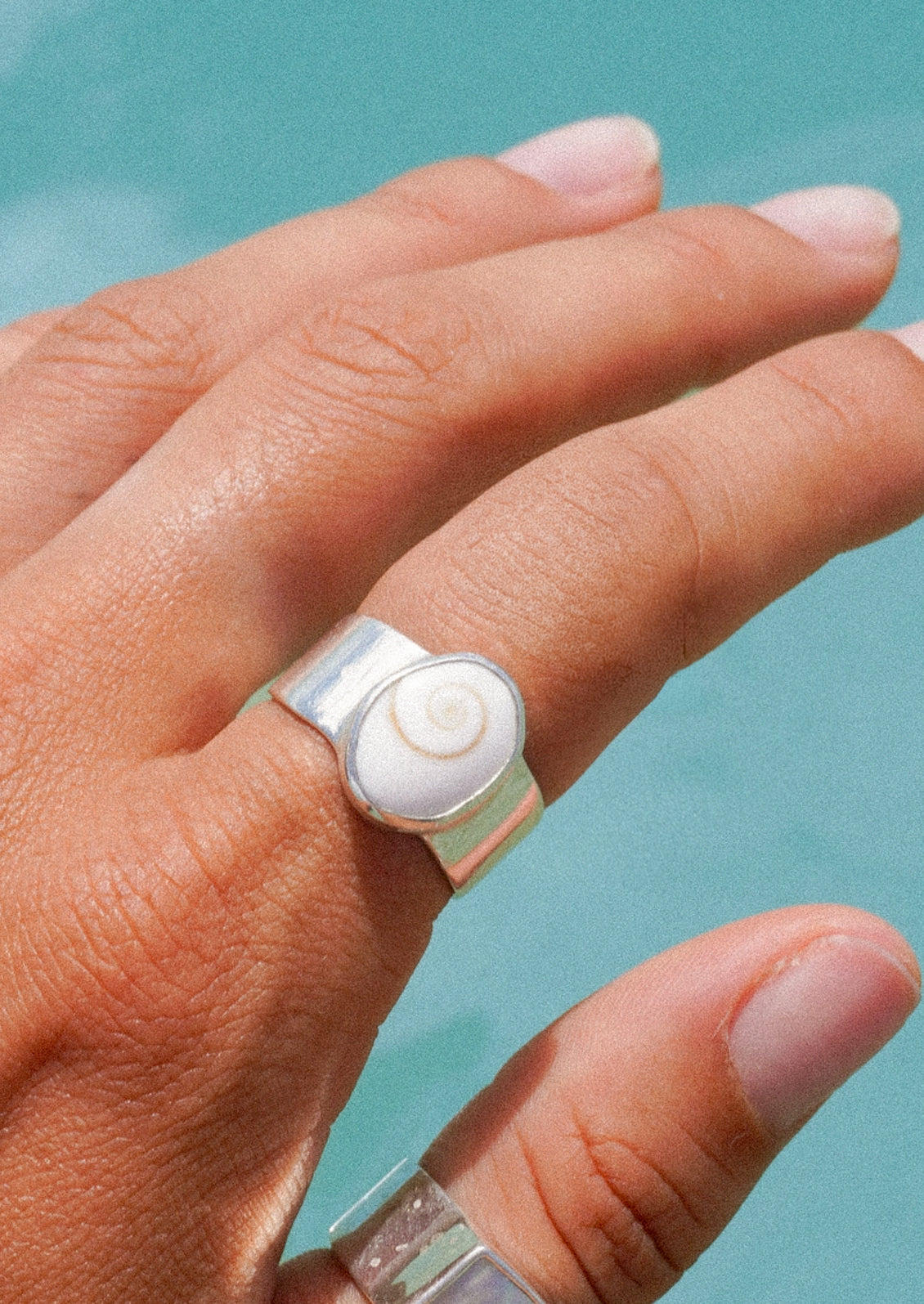 A hand with a thick silver ring with a shell signet.