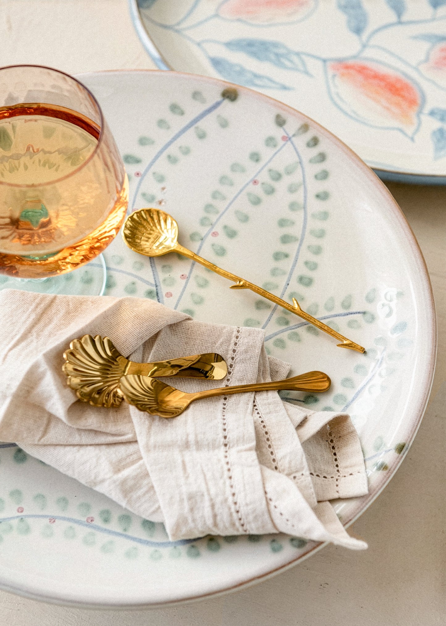 Table setting with gold spoons, a glass of rose, and decorative plates.