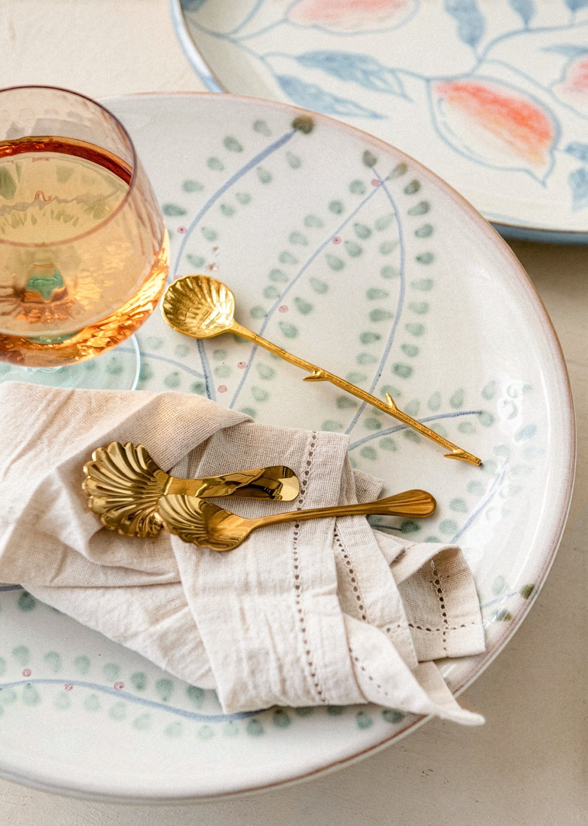 Table setting with gold spoons, a glass of rose, and decorative plates.