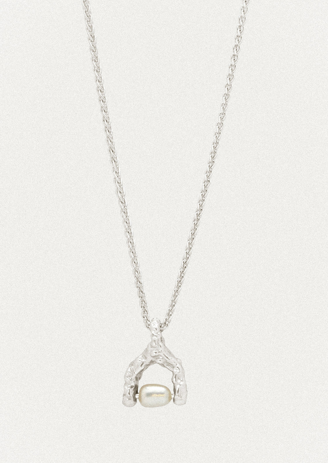 A sterling silver necklace with a wishbone-shaped charm that has a keshi pearl attached in the center.