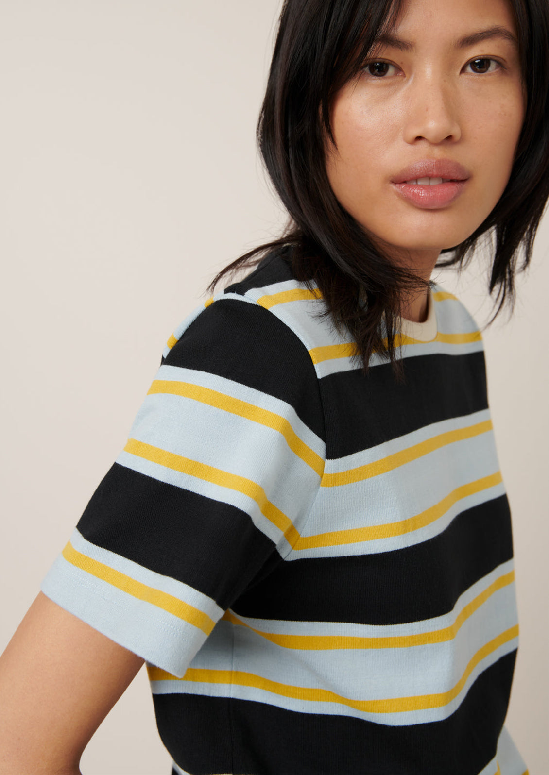 A person wearing a t-shirt with light blue, black and yellow rugby stripe pattern.