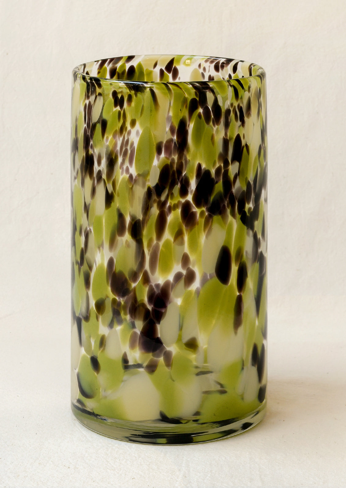 A cylindrical heavy glass vase with green and brown speckle pattern.