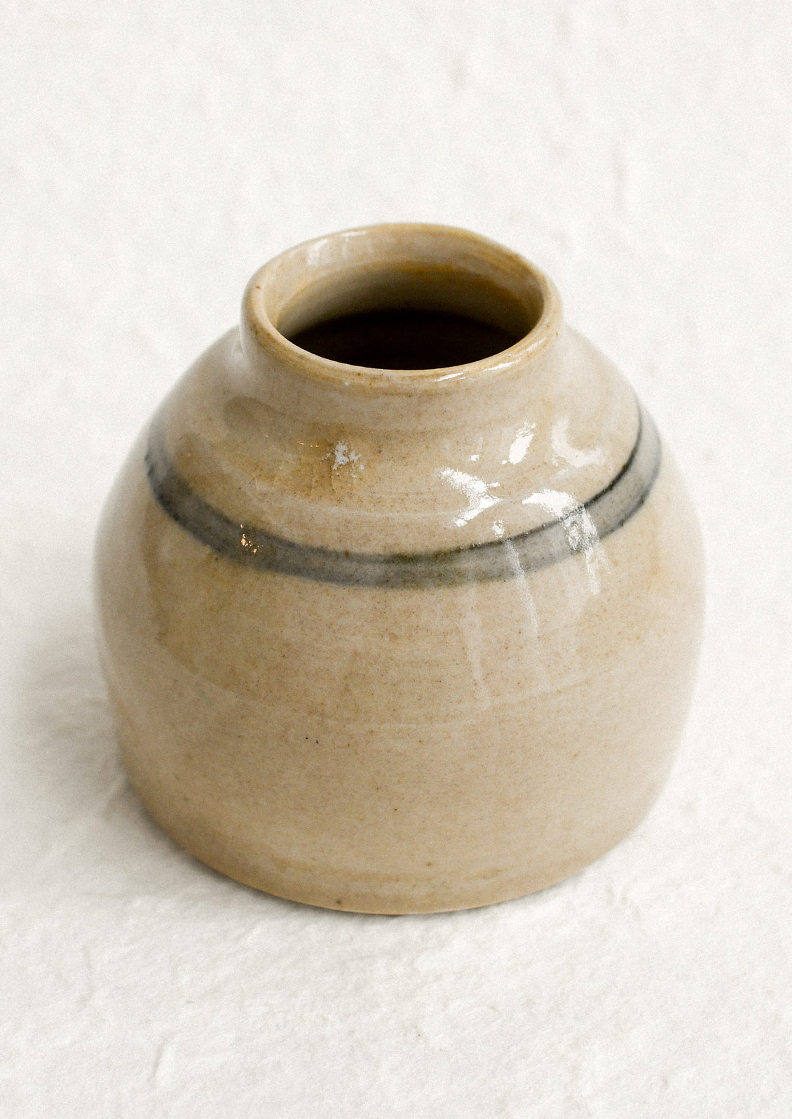 A small antique jar in beige with greyish blue stripe.