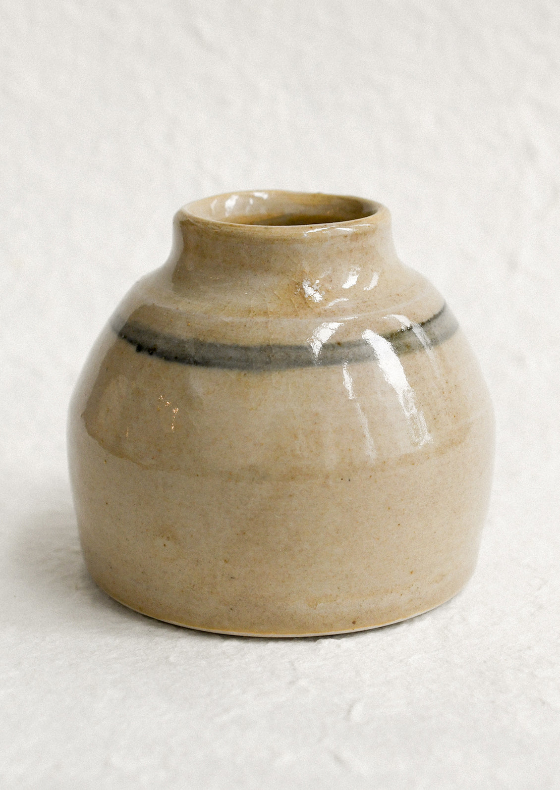 A small antique jar in beige with greyish blue stripe.