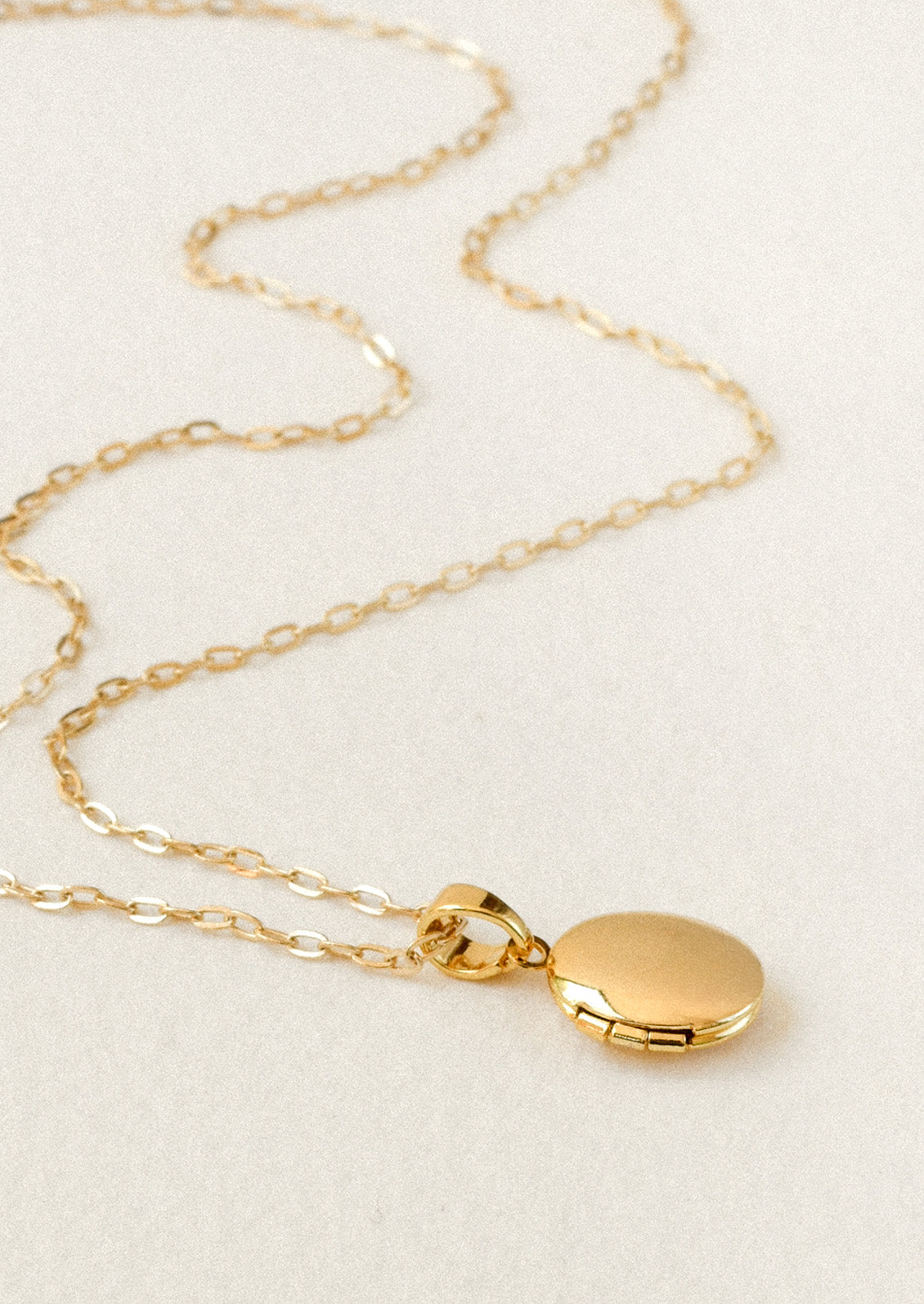 A gold chain necklace with a small oval locket pendant on a white background.