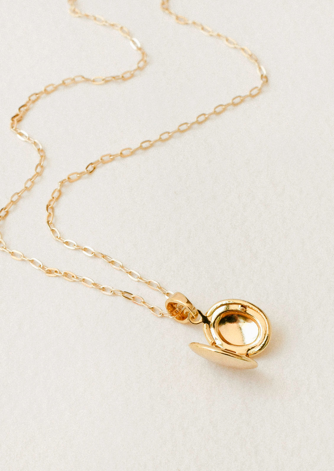 A gold chain necklace with a small opened oval locket pendant on a white background.