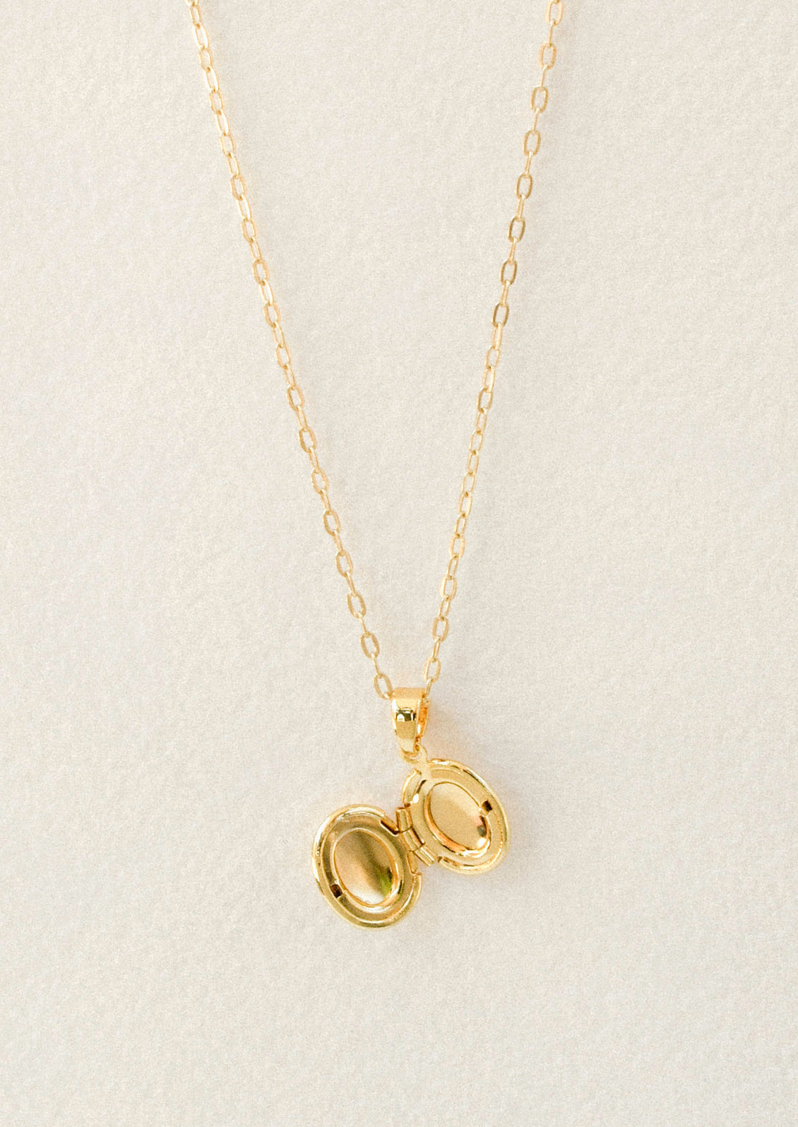 A gold chain necklace with a small opened oval locket pendant on a white background.