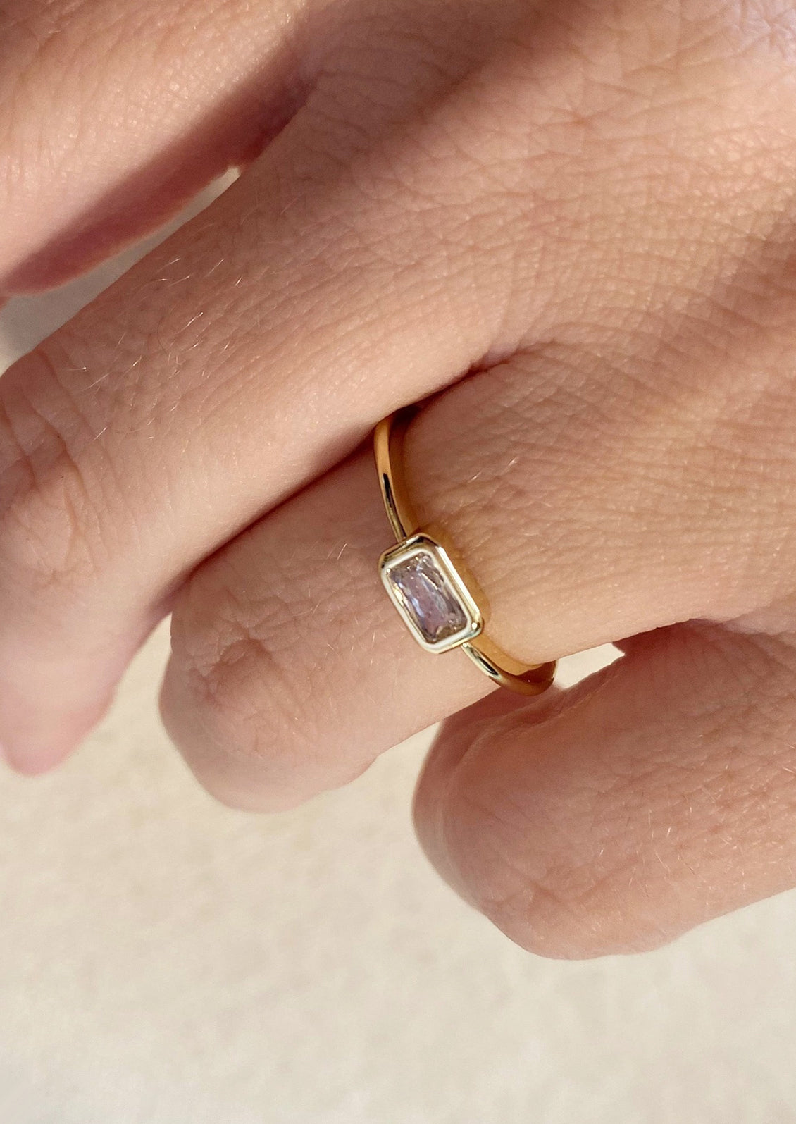 A gold ring with single rectangular clear stone.