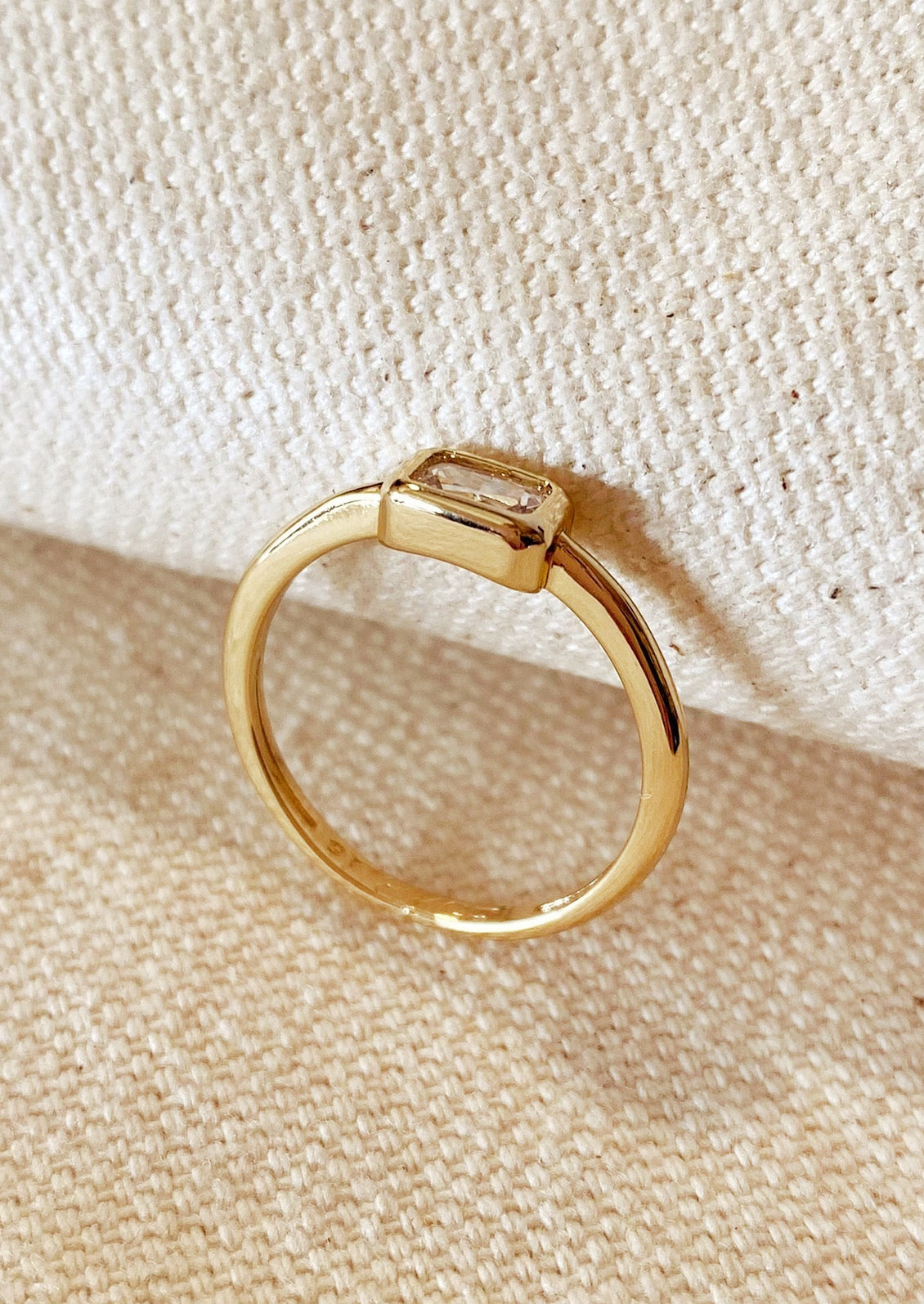 A gold ring with single rectangular clear stone.