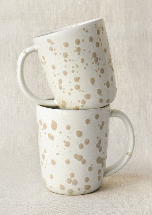 Two white mugs with a brown paint splatter design stacked on top of each other.