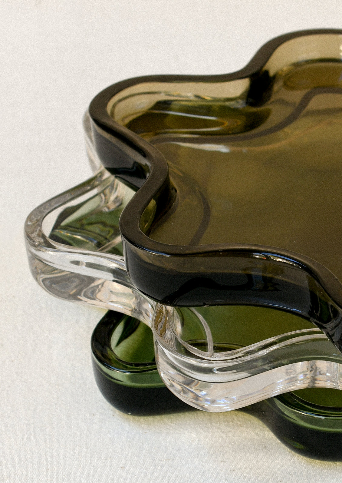 A stack of clear glass trays in a squiggle shape in coffee, clear, and olive.
