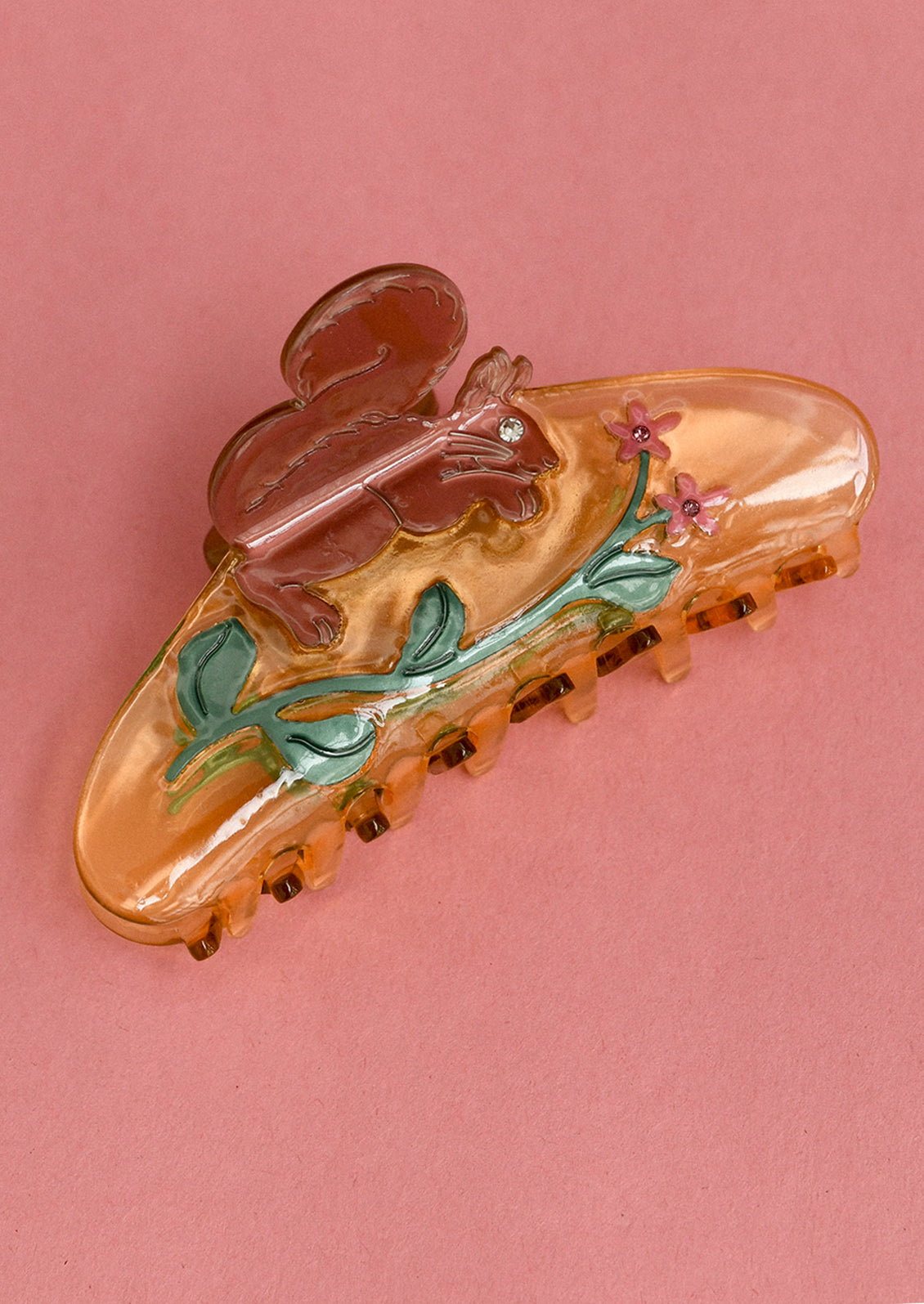 A hair clip in orange with squirrel and flower motif.