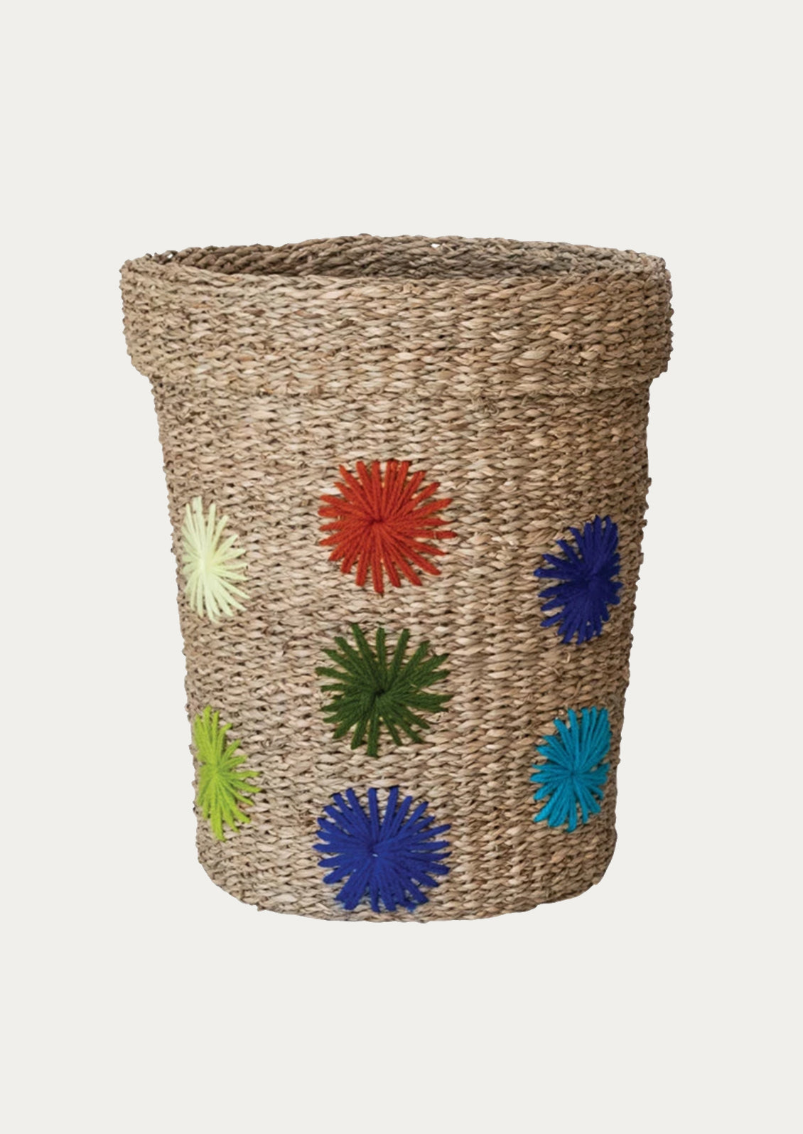 A natural seagrass storage basket with multicolor embroidered wool starburst pattern.