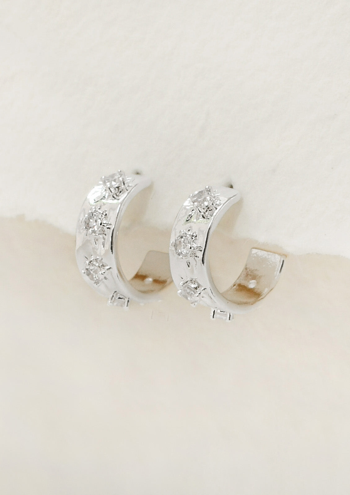 A pair of small silver plated hoop earrings with raised crystal starbust pattern.