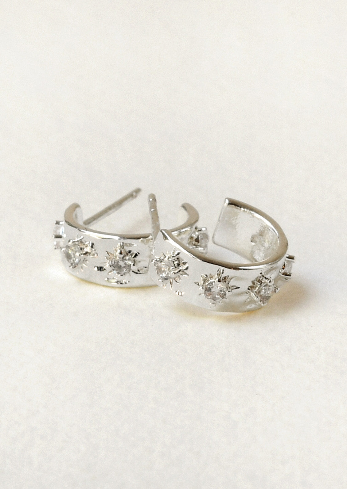 A pair of small silver plated hoop earrings with raised crystal starbust pattern.