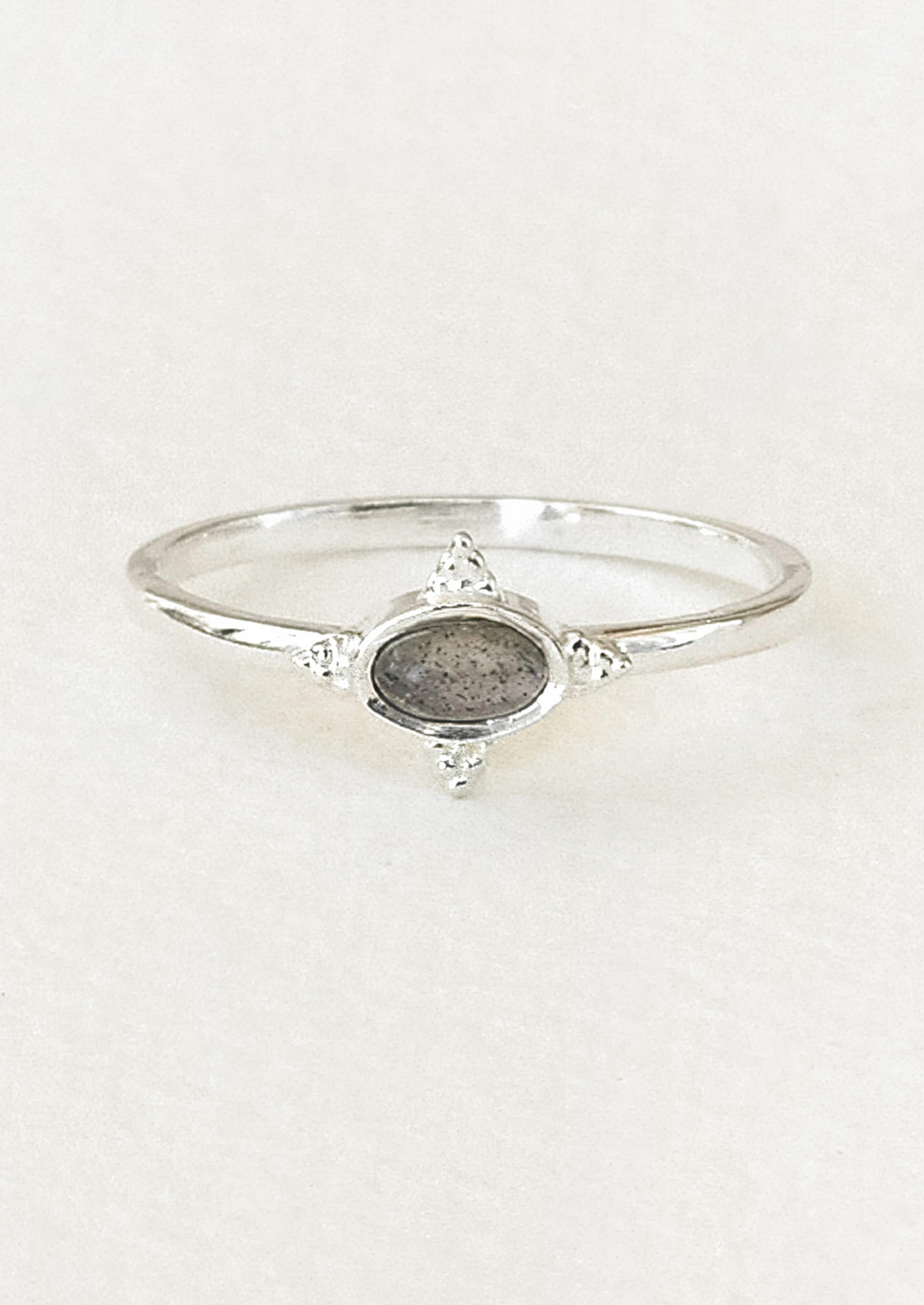 A sterling silver ring with a dark grey oval labradorite stone framed in a star shaped setting on a white paper.