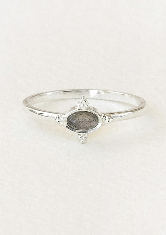 A sterling silver ring with a dark grey oval labradorite stone framed in a star shaped setting on a white paper.