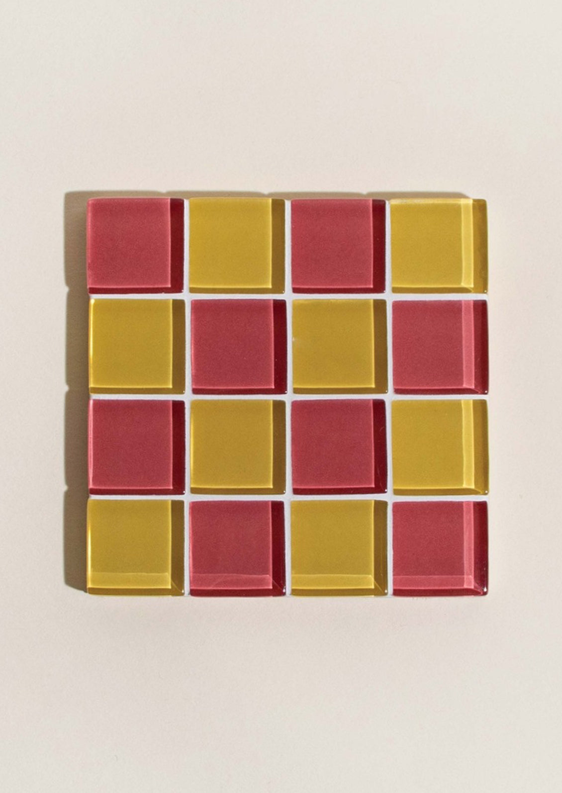 A glass tile coaster in two tone checker pattern in yellow and strawberry.