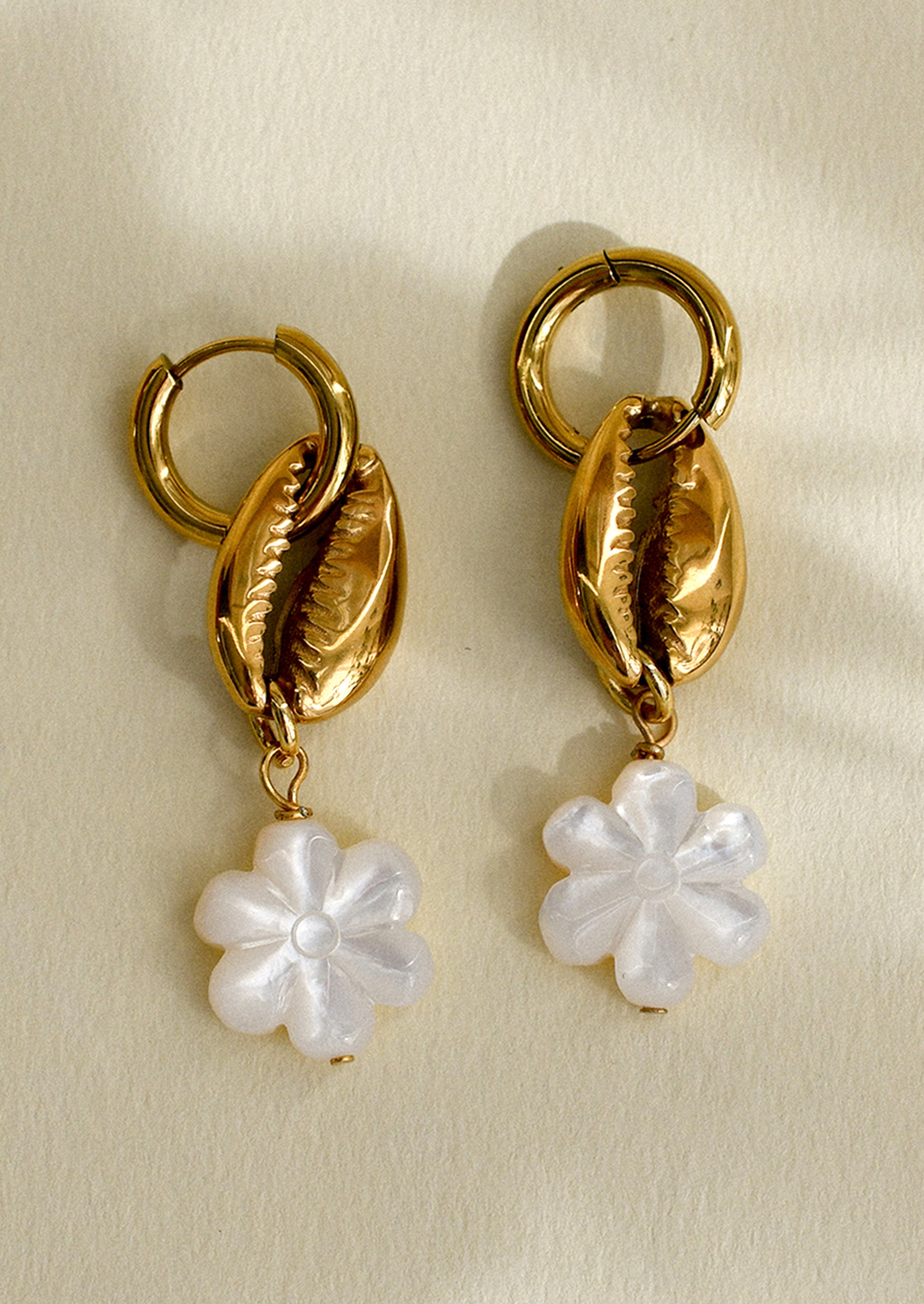 A pair of huggie hoop earrings with gold conch shell and mother of pearl flower charm.