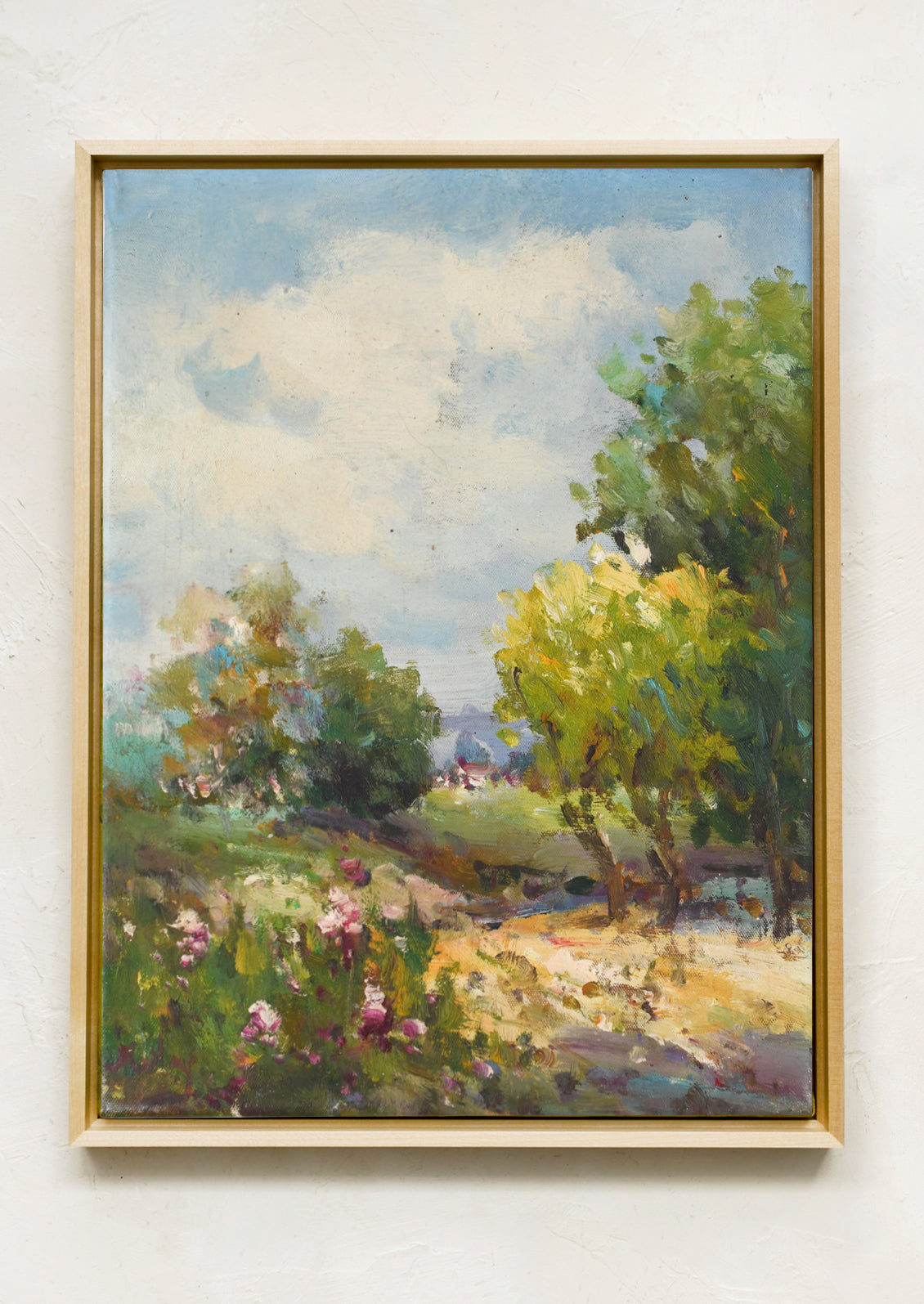 An oil painting depicting a painterly meadow landscape scene, with a blue sky. Framed in a minimal, natural maple frame.