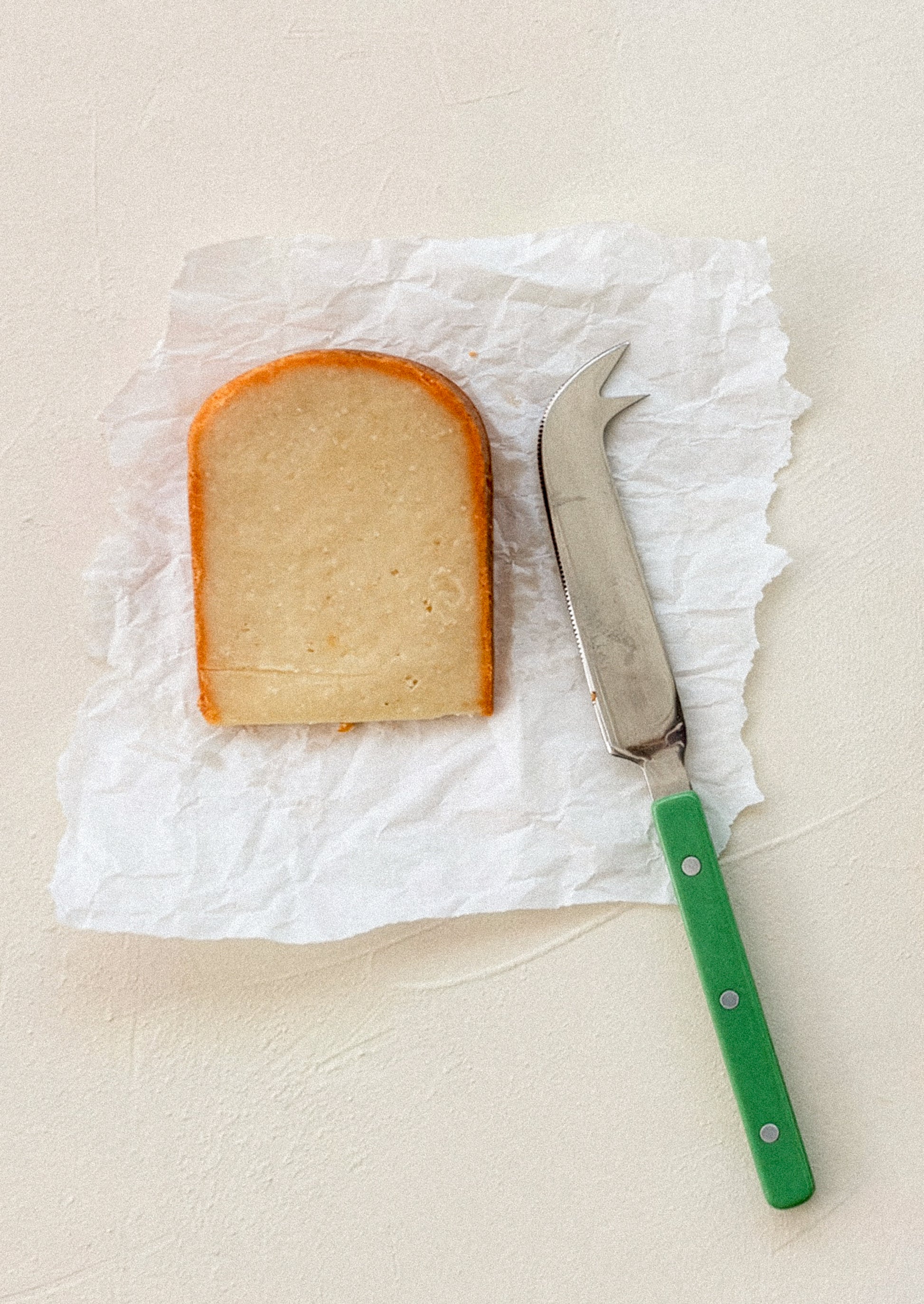 Slice of bread on paper with a knife next to it on a beige background