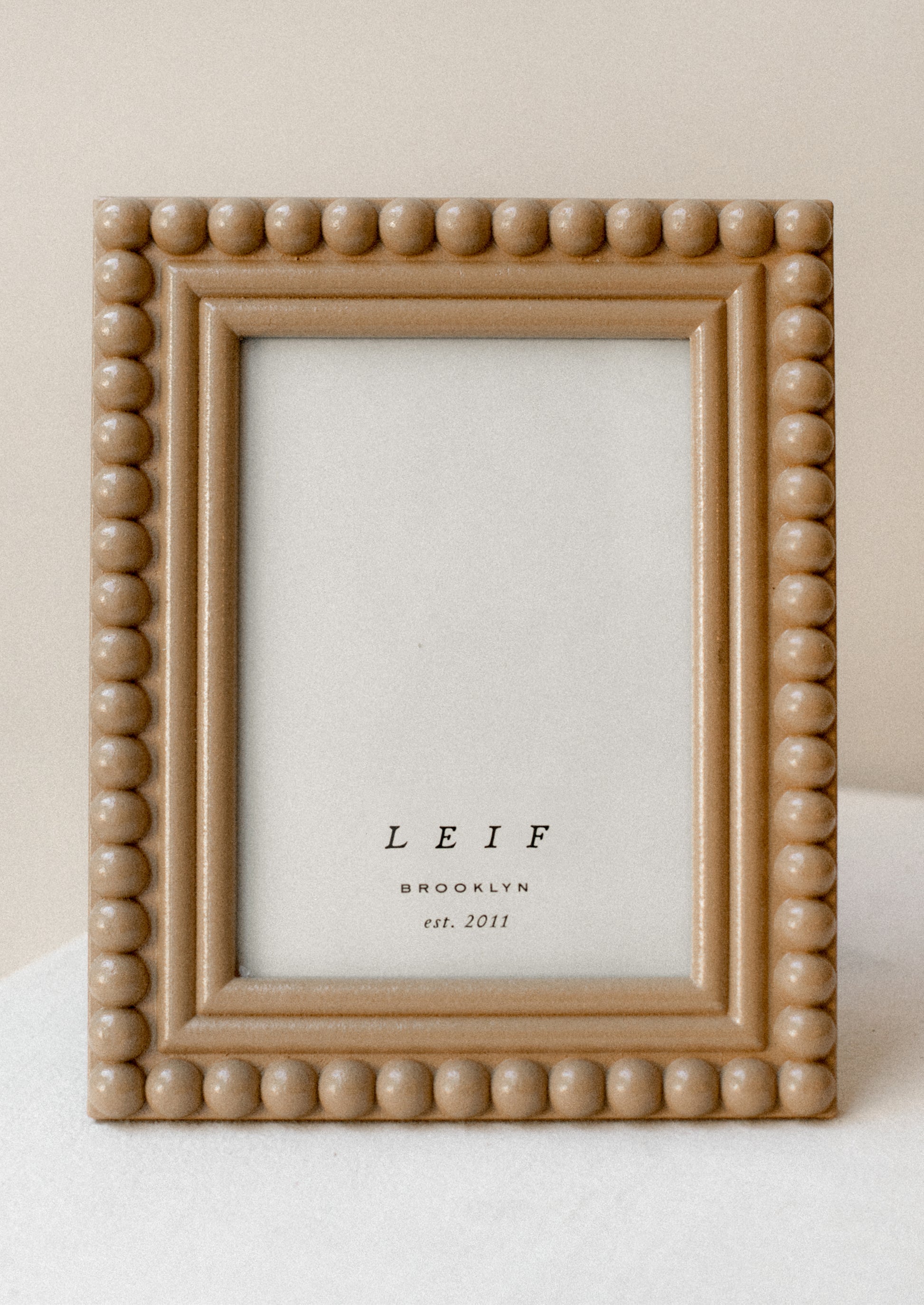 A picture frame with hobnail border in camel colored lacquer.