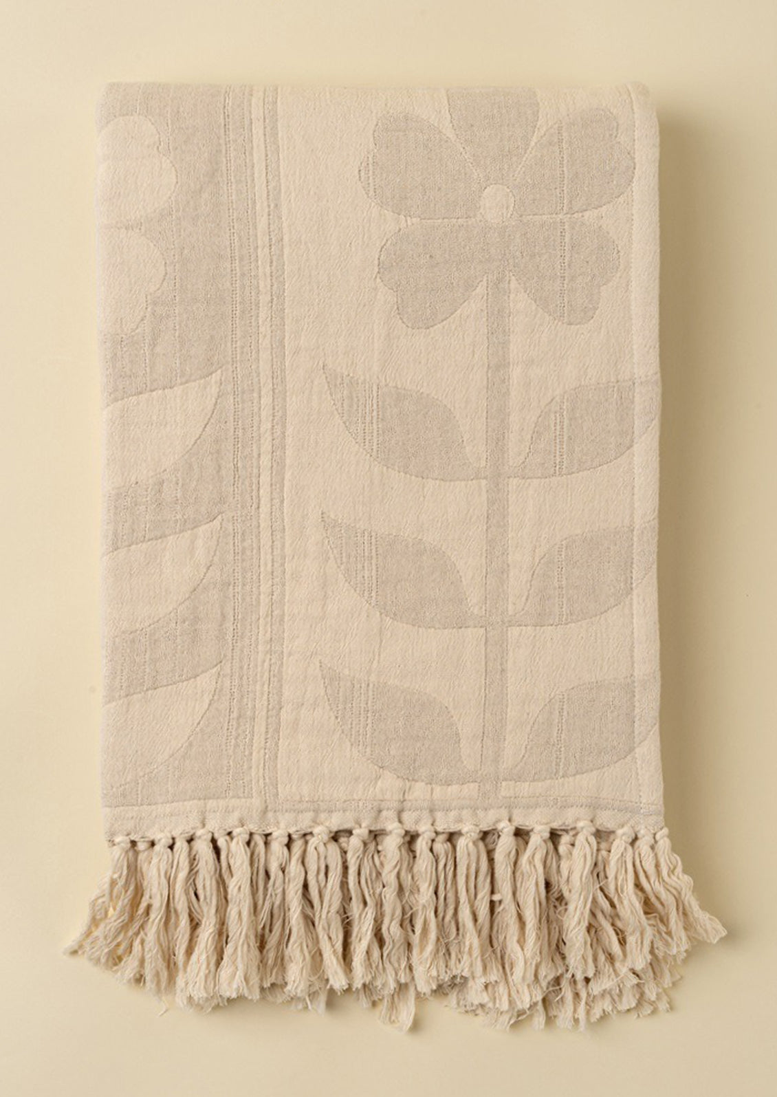 Floral patterned throw in tan and cream with tassel trim.