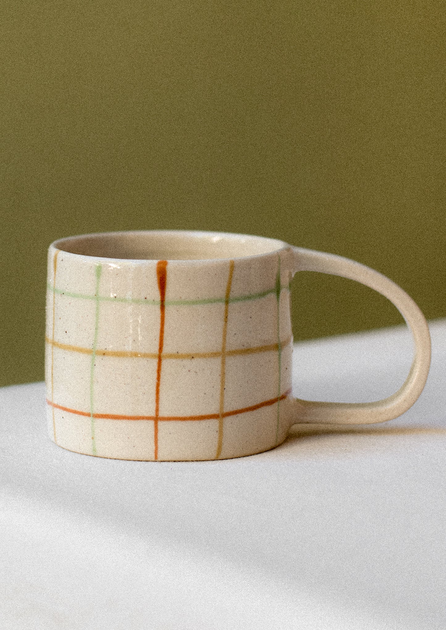 A ceramic mug in natural cream clay with rust and mint check pattern.