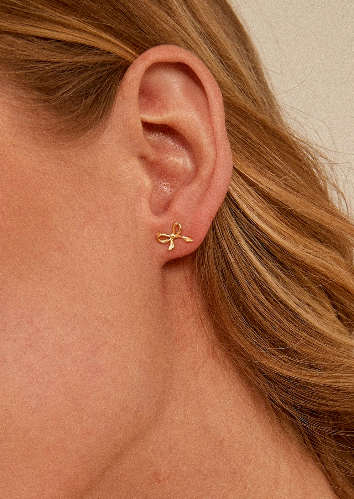 A pair of small stud earrings in gold, in the shape of a small bow.