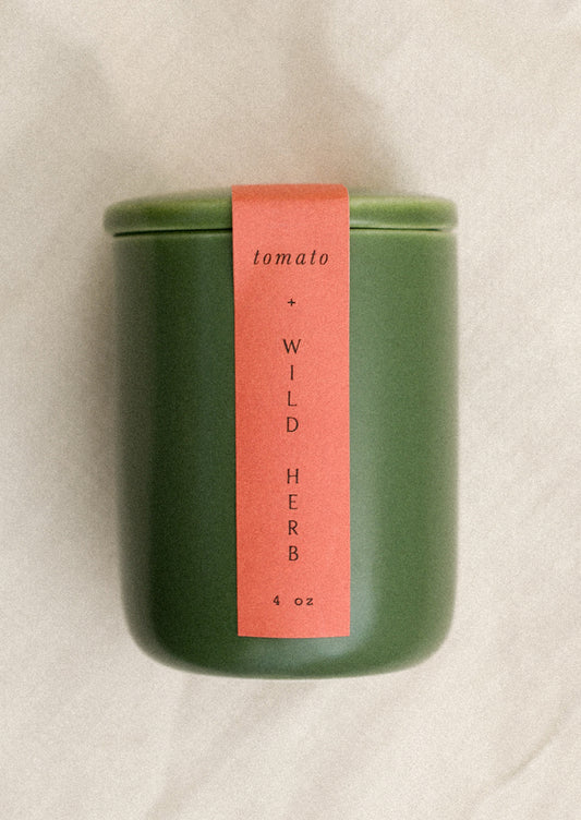 A small candle in lidded green ceramic jar in Tomato & Wild Herb scent.