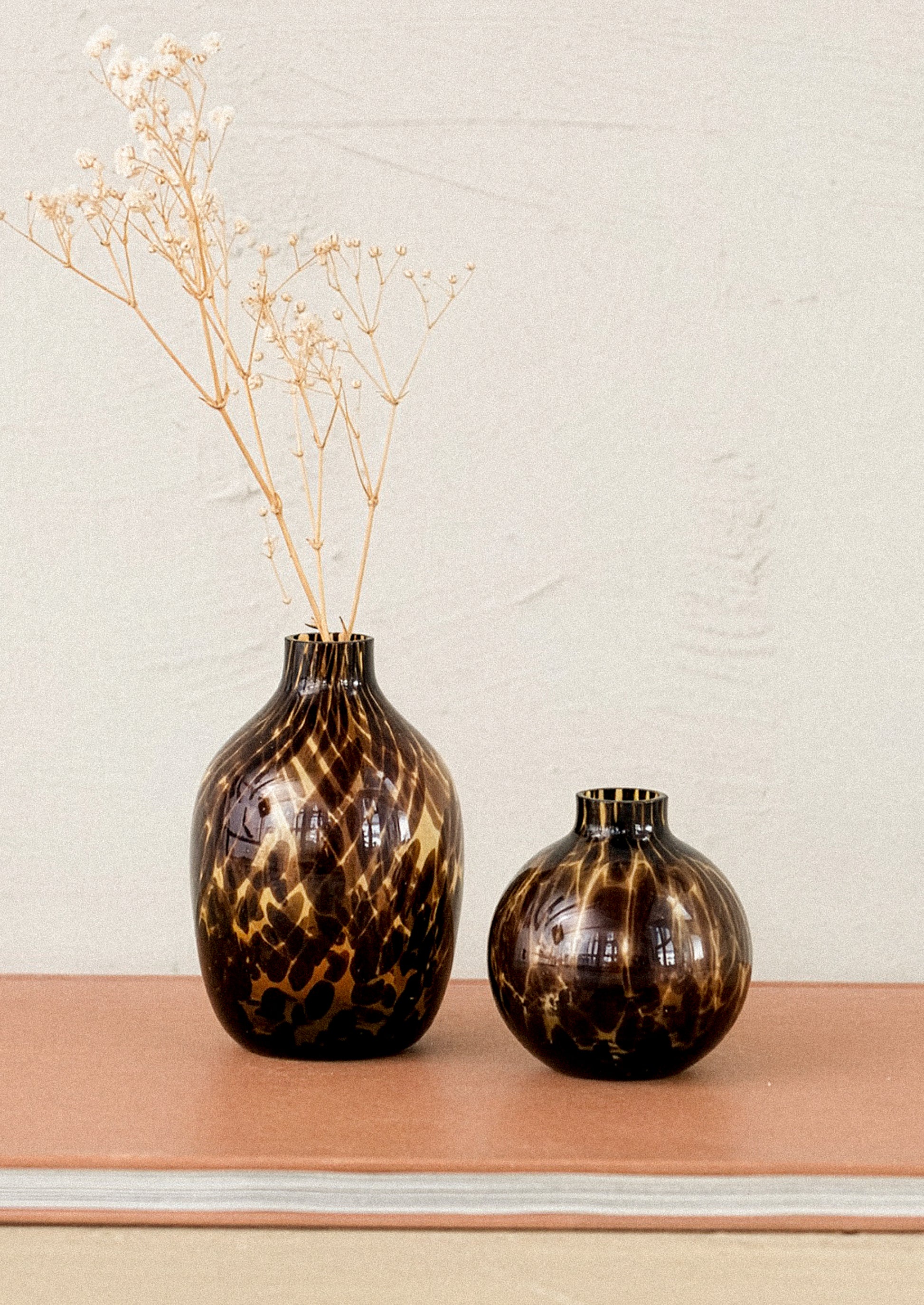 Two tortoiseshell-patterned vases on a wooden surface with a light background