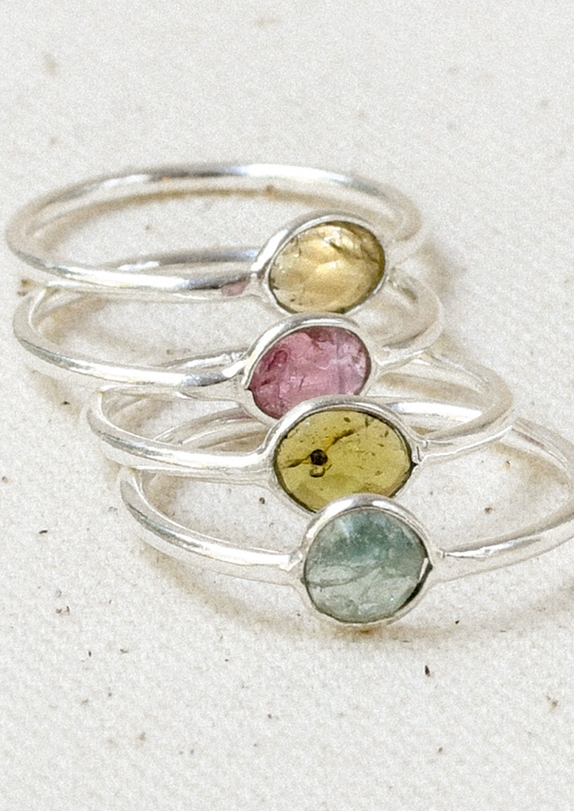 Four sterling silver rings stacked on top of one another with natural tourmaline stones in varying colors.